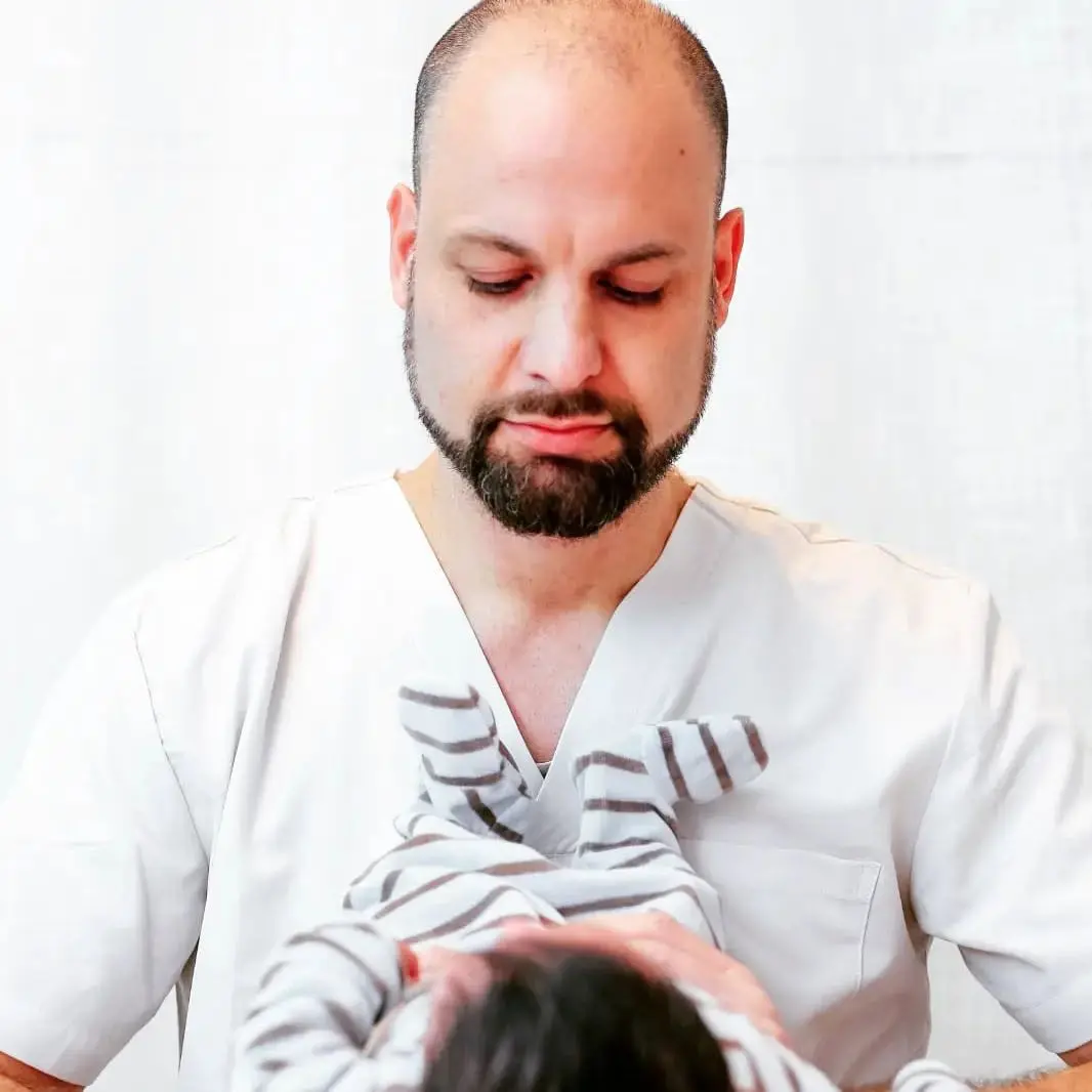 נתן מחזיק תינוק בעדינות, הבעה רגועה